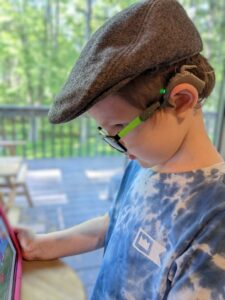 A boy reads using glasses connected to his cochlear processor by an adapter.